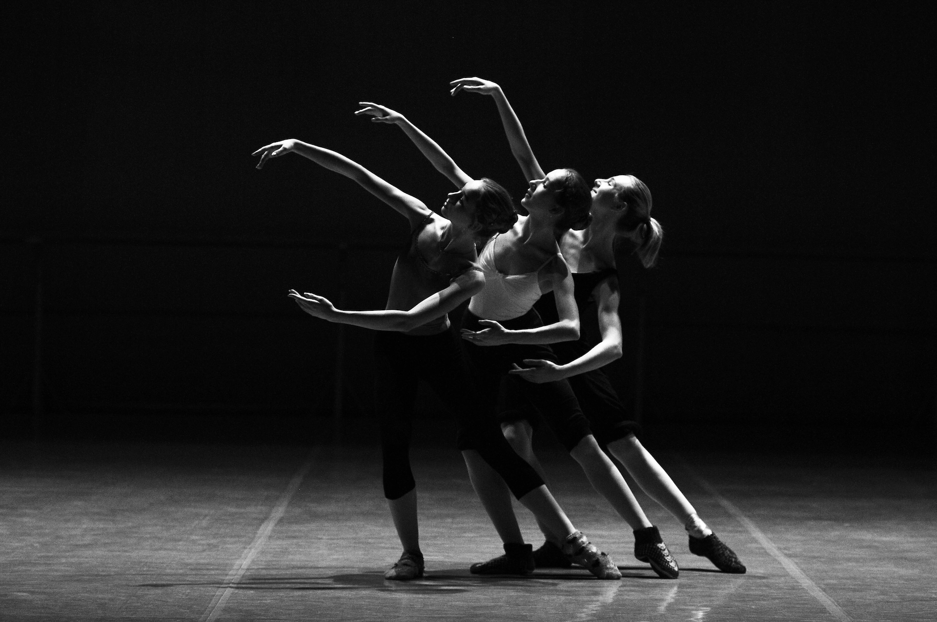 Three dancers reaching upward under stage lights